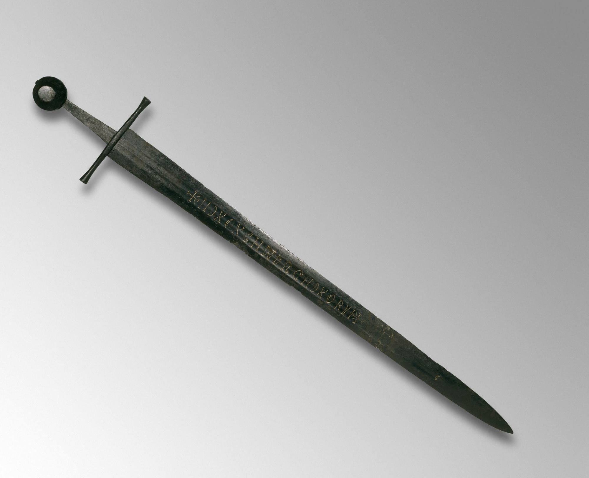 The Witham Sword, British Museum 1858,1116.5. Full view of double-edged steel blade with cross guard and wheel pommel, gold wire inscription visible on the blade.